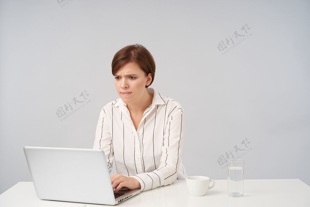 办公室年轻漂亮的棕色头发的女士 留着时髦的短发 双手放在键盘上 坐在白色的椅子上 焦急地看着笔记本电脑的屏幕桌子困惑女商人