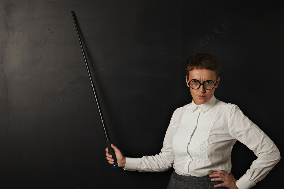 讲师愤怒的女老师和显示在她身后的黑色粉笔板与折叠指针棍子指看