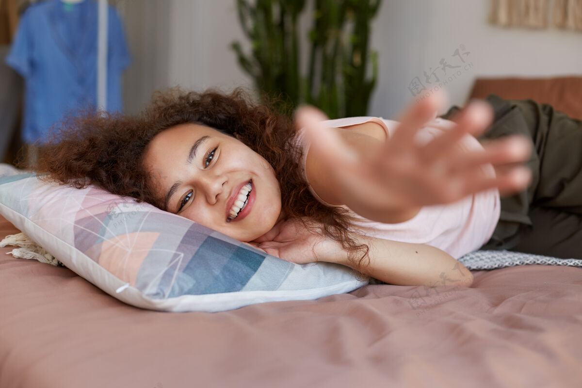 青少年年轻的黑皮肤女人躺在床上享受阳光明媚的一天在家里 面带微笑 看起来快乐和喜悦高兴休息美国