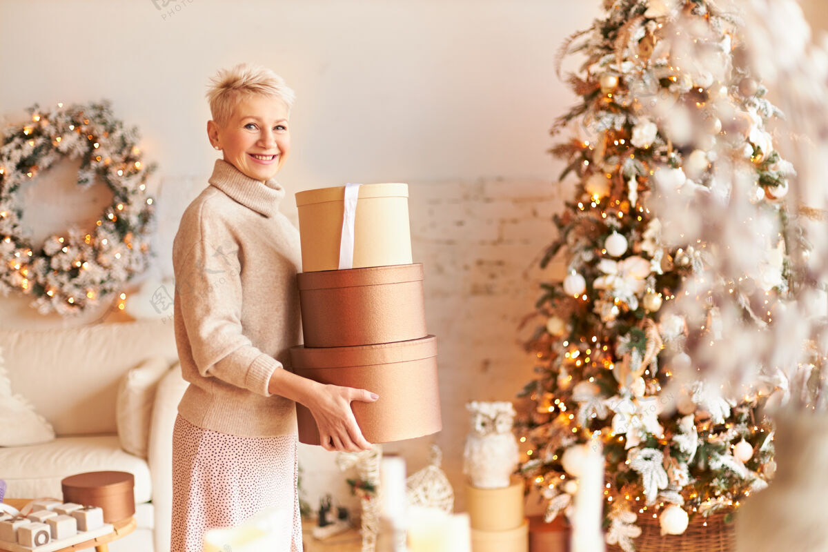 节日室内拍摄的是一位快乐优雅的中年女性 金发短发 站在装饰过的客厅里 手里拿着装满礼物的盒子 准备把它们藏起来直到圣诞节新年快乐圣诞老人肖像成人