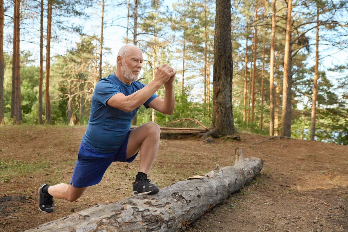 运动帅气精力充沛的老人 留着胡子 穿着运动服 在野外做有氧运动老人有着快乐自信的神情 脚踩木头 跑步前锻炼腿部肌肉活动森林原木