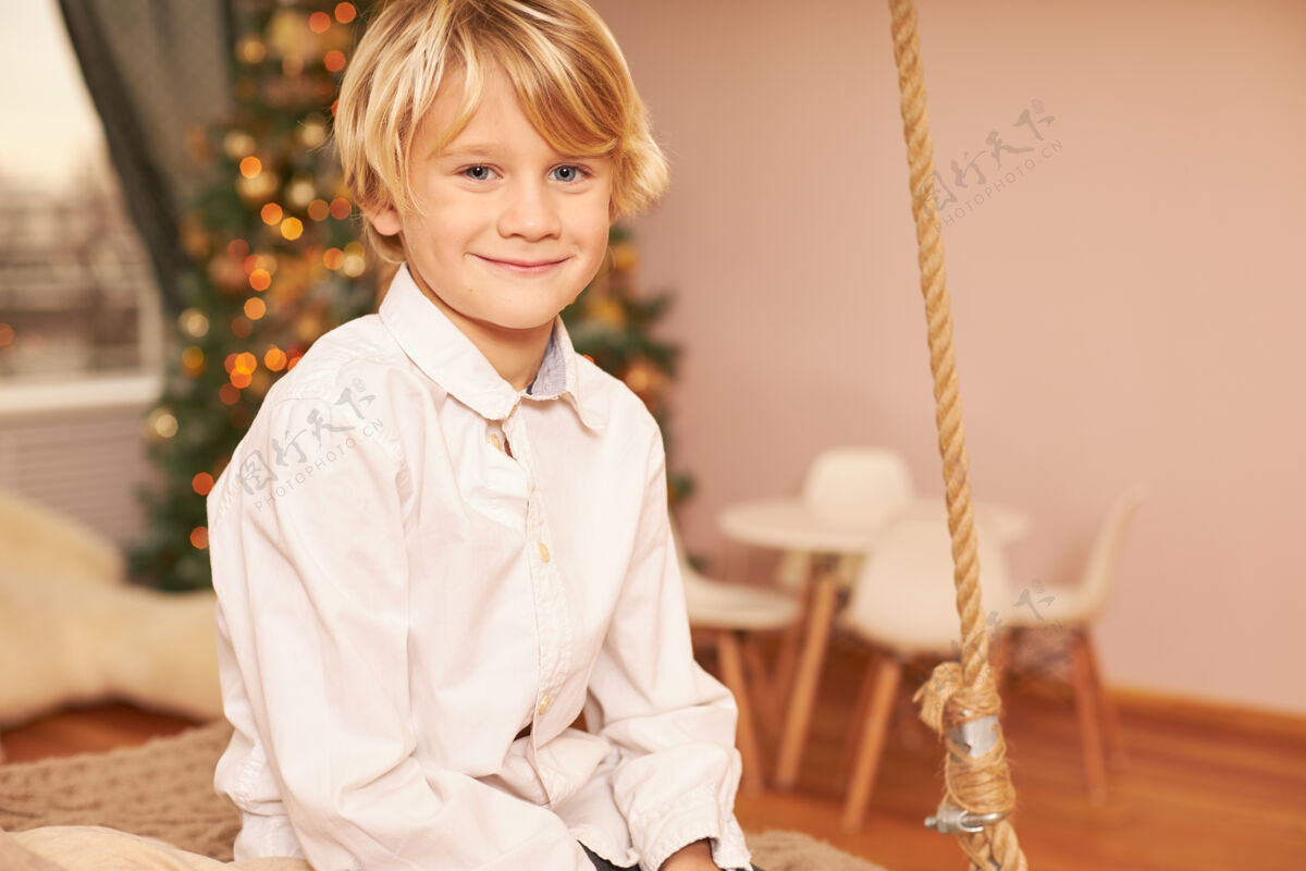 孩子穿着白衬衫的可爱欧洲男孩的肖像 享受着节日的气氛 期待着平安夜 坐在装饰着新年树的客厅里 开心地微笑着孩子肖像微笑