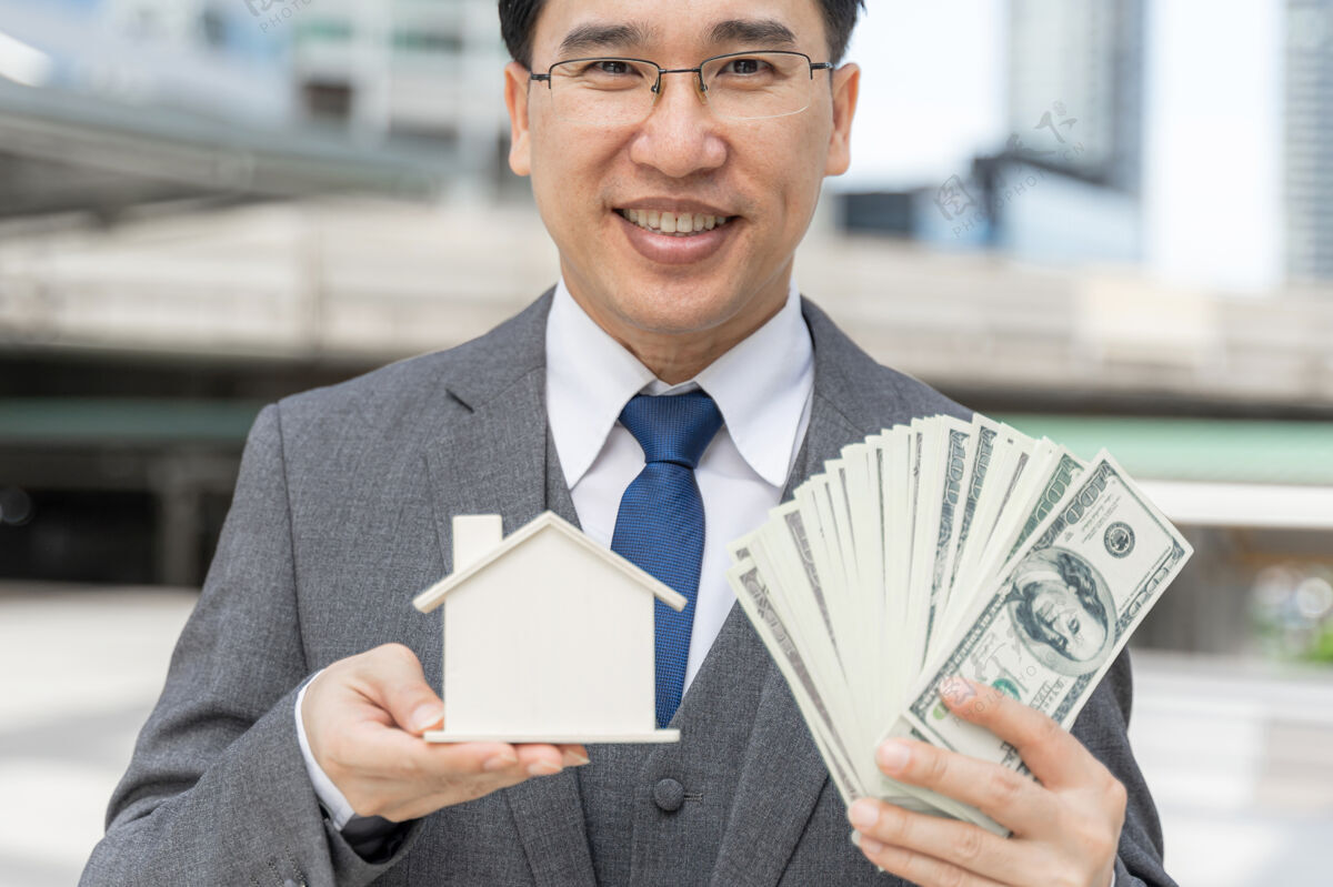 商人肖像亚洲商人拿着美元钞票和模型房子在商业区投资房屋贷款家庭房屋