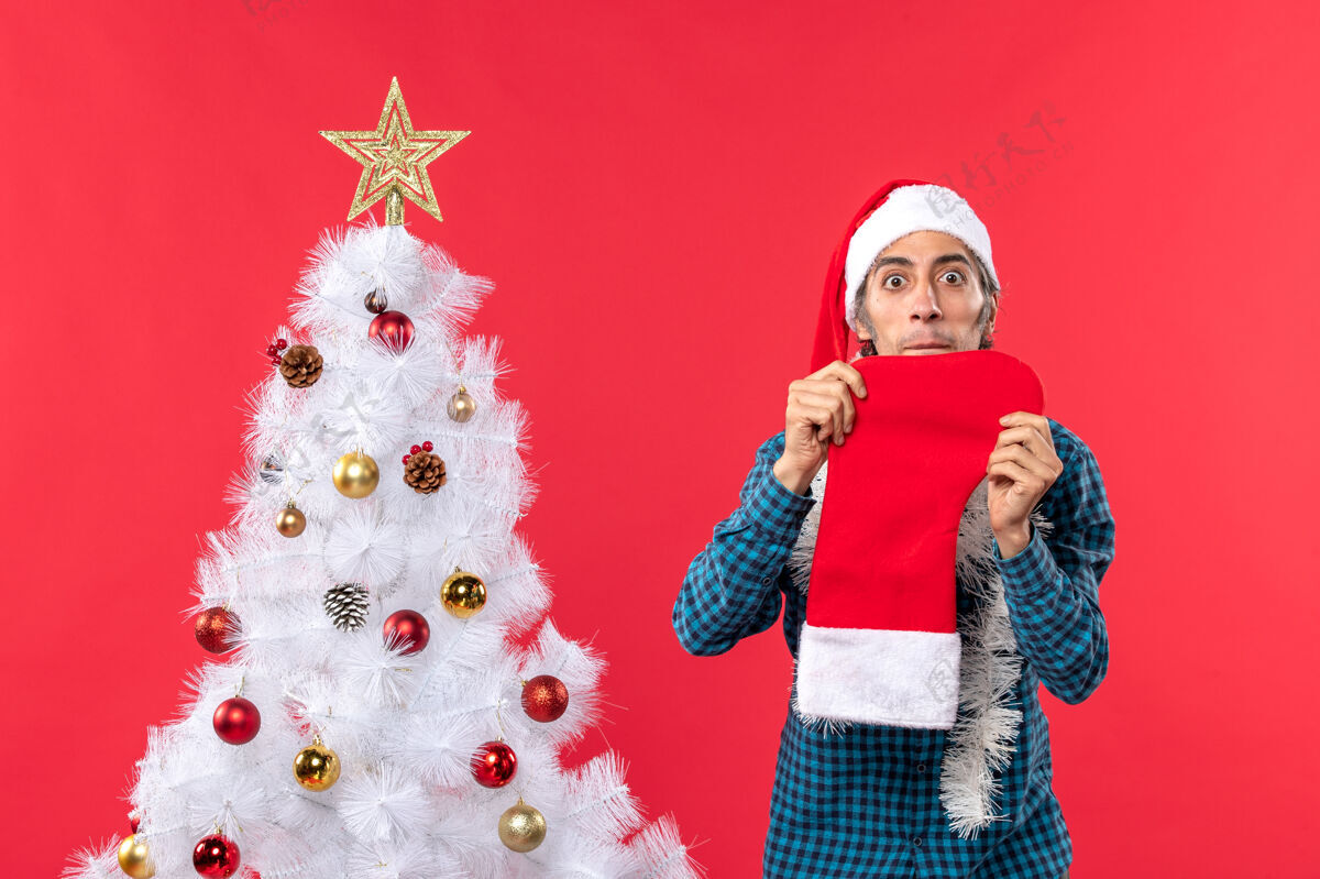 雪人一个戴着圣诞老人帽子 穿着蓝色条纹衬衫 展示圣诞袜子的悲伤的年轻人庆祝年轻悲伤