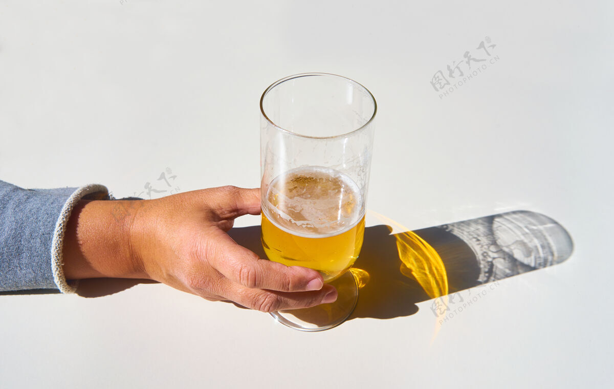 饮料女人的手拿起一杯啤酒 影子倒映在白色的桌子上玻璃杯白色泡泡