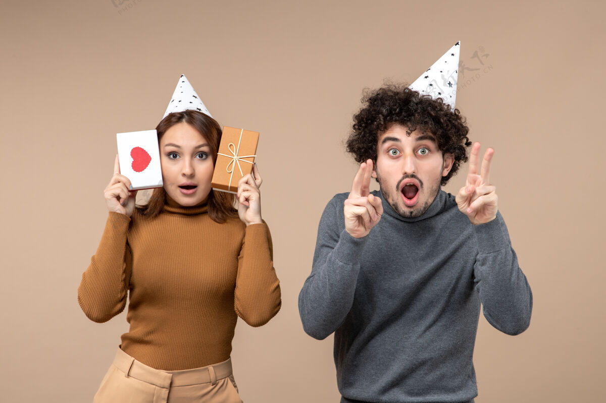 男人新年概念与年轻夫妇戴新年帽女孩的心和礼物和家伙显示两个灰色礼物心情侣