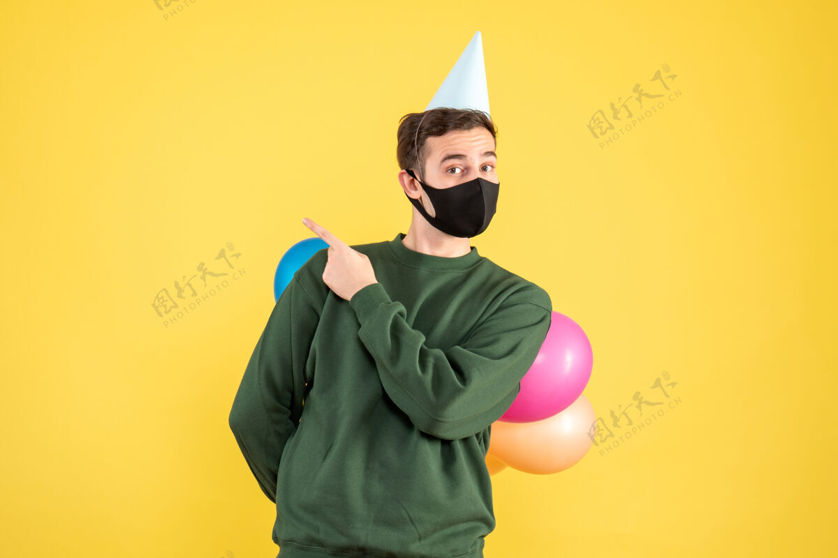 艺术正面图：戴着派对帽的年轻人 背着彩色气球站在黄色的地板上面具五颜六色聚会