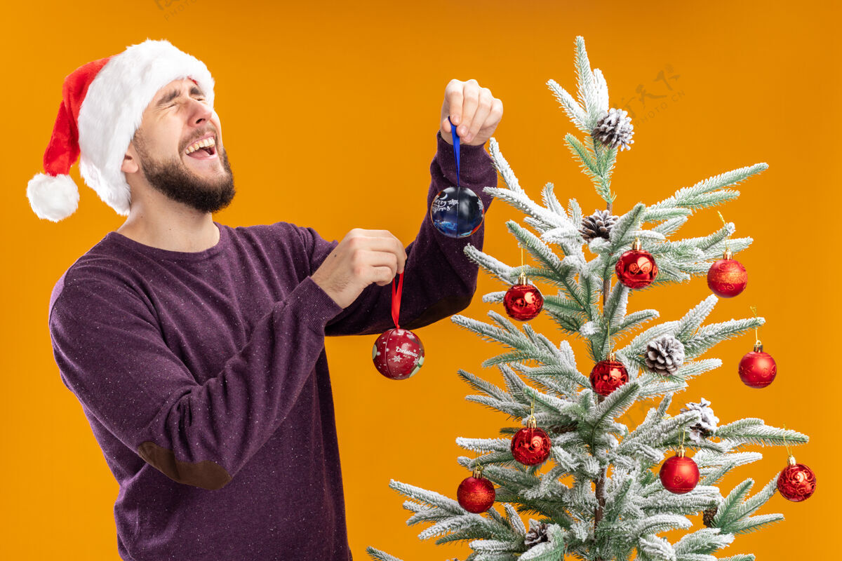 玩具穿紫色毛衣戴圣诞帽的年轻人把玩具挂在圣诞树上年轻人圣诞树帽子