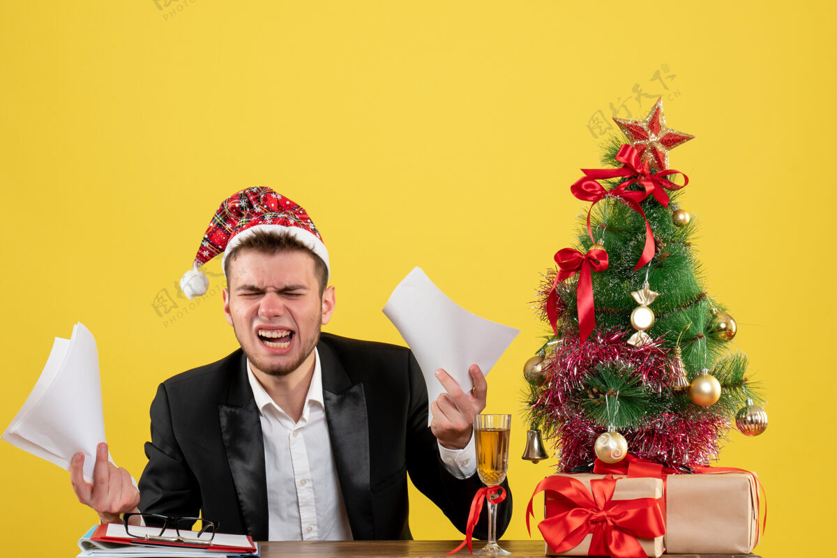 工作正面图：男工人坐在他工作的地方后面 黄色办公桌上放着文件 办公室新年彩色圣诞工作颜色圣诞节座位