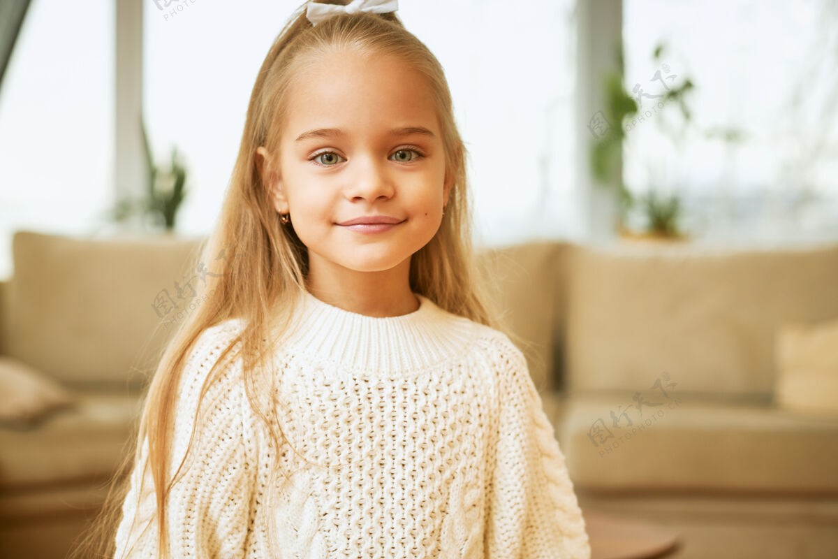 可爱孩子 美丽 时尚漂亮的白人小女孩 蓝眼睛 可爱的微笑 长发 穿着舒适的白色套头衫 在客厅里摆姿势 心情愉快 看起来很快乐毛衣微笑孩子