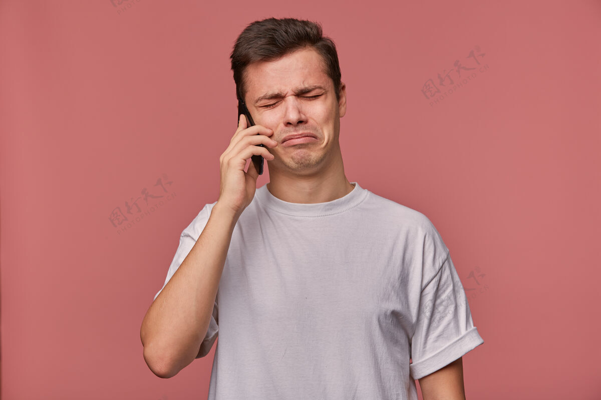 粉色一个穿着白t恤的悲伤的年轻人的画像 他在电话里说 听到坏消息 站在粉红色的地面上 表情很不高兴悲伤不高兴肖像