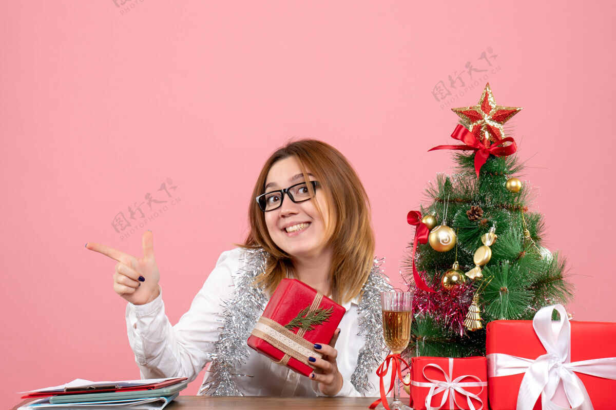 粉红色女工人坐在粉红色的圣诞礼物和圣诞树旁的正视图女工人工人工作