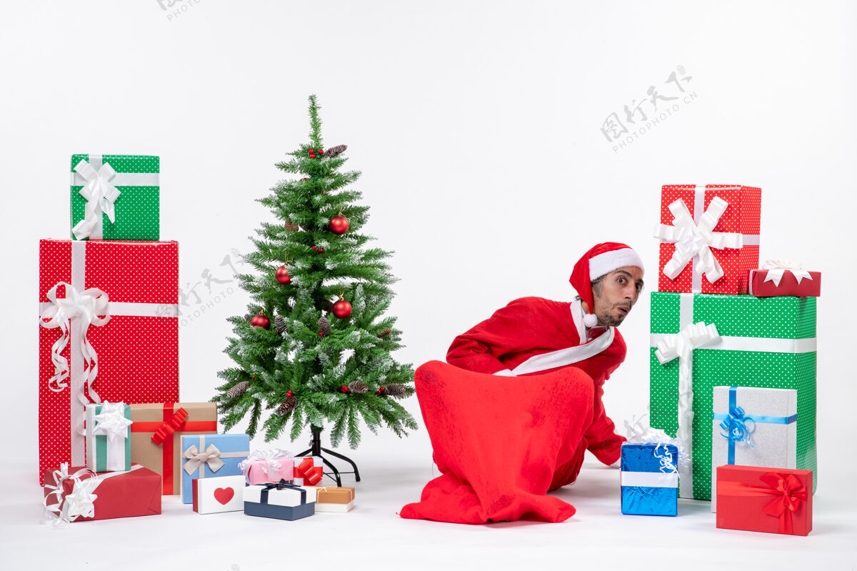 圣诞老人年轻人打扮成圣诞老人 拿着礼物和装饰好的圣诞树坐在地上找东西圣诞老人打扮礼物