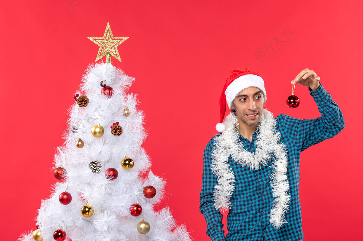 衬衫困惑的年轻人戴着圣诞老人的帽子 穿着蓝色条纹衬衫 展示着装饰饰品配件圣诞圣诞老人