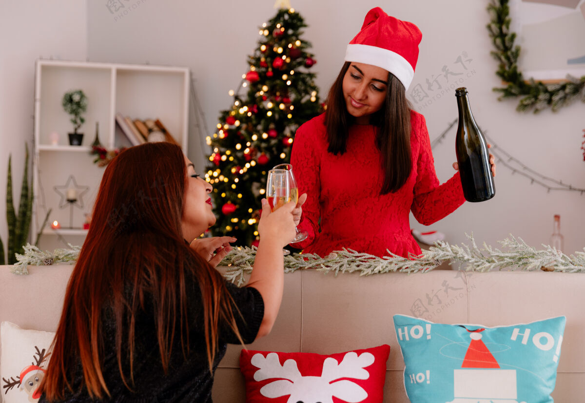 家高兴的女儿和母亲坐在沙发上碰杯香槟在家享受圣诞节的时光杯子母亲享受