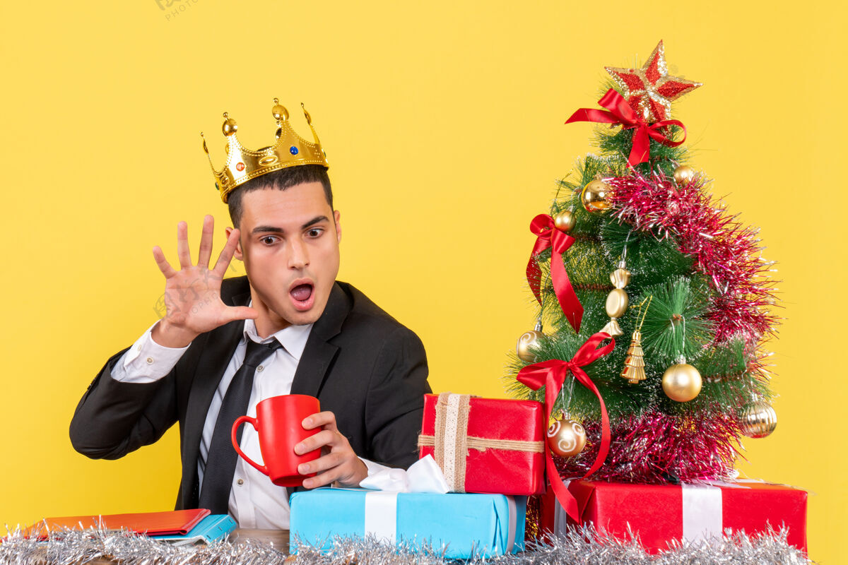 套装正面图惊讶的戴着皇冠的男人看着圣诞树旁的杯子和礼物微笑礼物惊讶