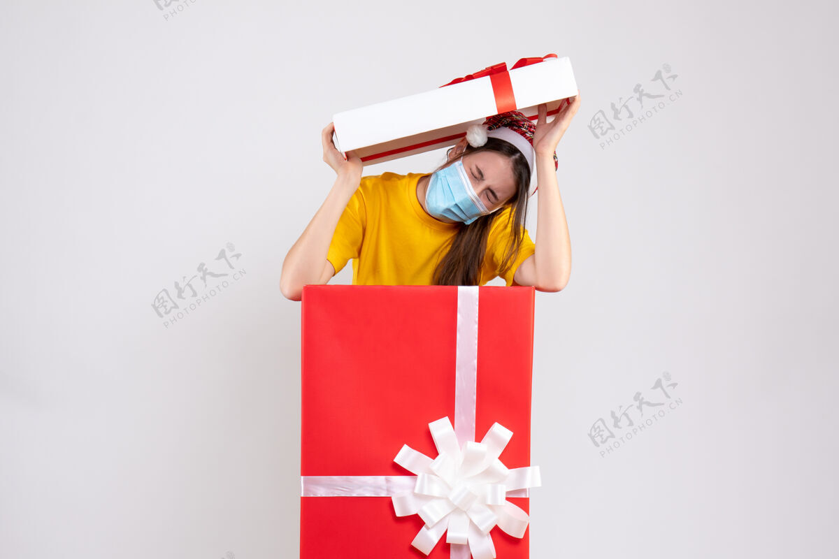 帽子一个戴着圣诞帽 头上戴着盒盖 站在白色圣诞礼物后面的吓坏了的女孩盒子放女孩
