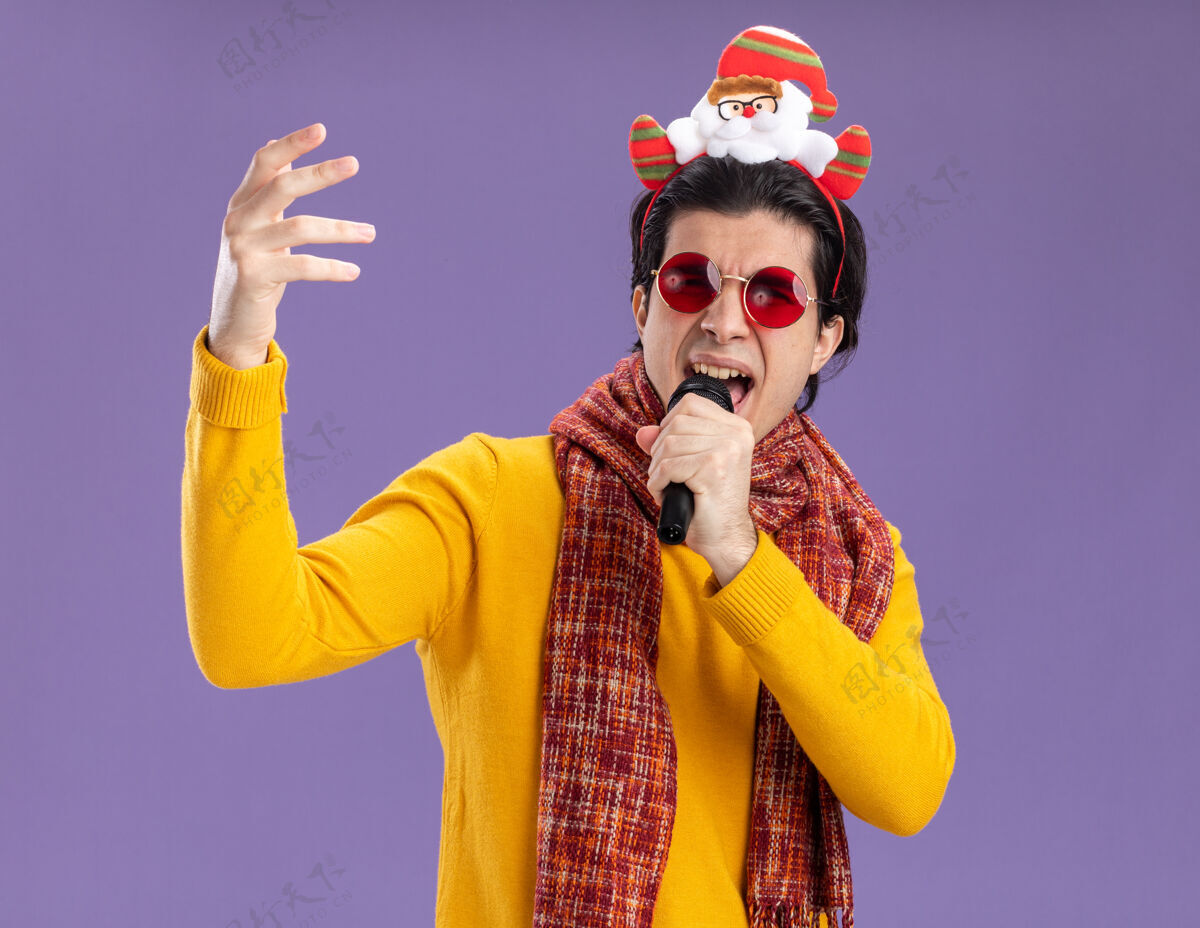 兴奋身穿黄色高领毛衣 脖子上围着暖和围巾 头上戴着滑稽镜框的年轻人手持麦克风 站在紫色的墙上兴奋地唱歌男人高领毛衣圣诞节