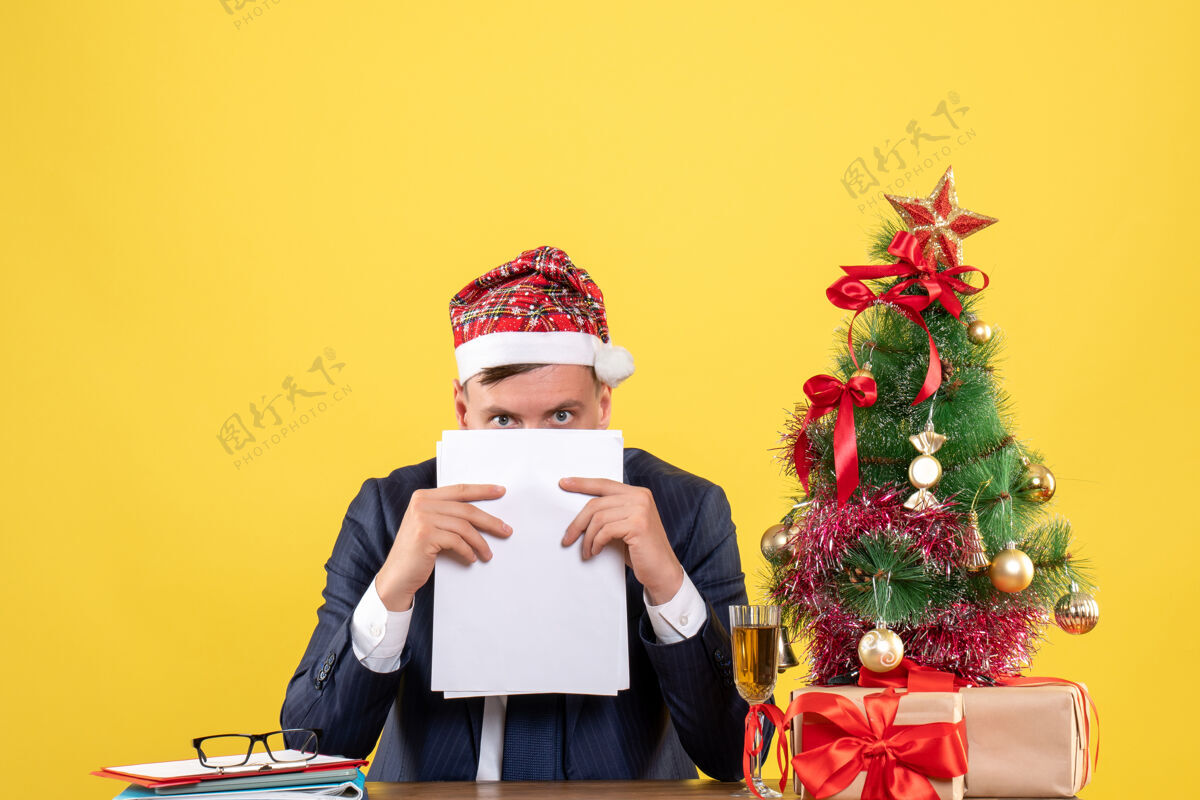 坐正视图撬人持有文件坐在圣诞树附近的桌子上 黄色的礼物黄色烟斗礼物
