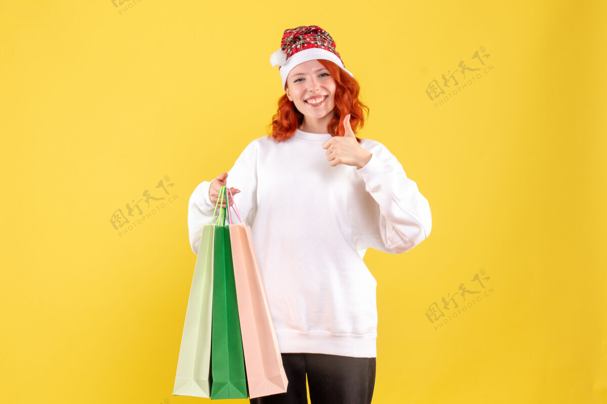 快乐黄色墙壁上拿着购物包裹的年轻女子的正视图女性节日女人