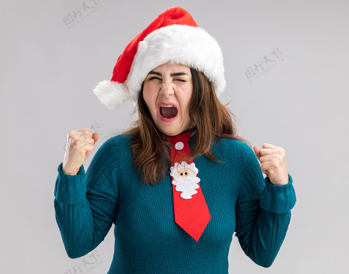领带恼怒的成年白人妇女戴着圣诞帽 打着圣诞领带 在白色背景上保持拳头孤立 留有复制空间圣诞老人大人恼火