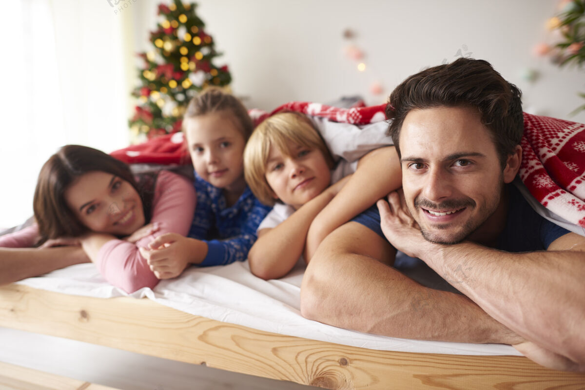 羽绒圣诞节时一家人躺在床上庆祝圣诞树圣诞树