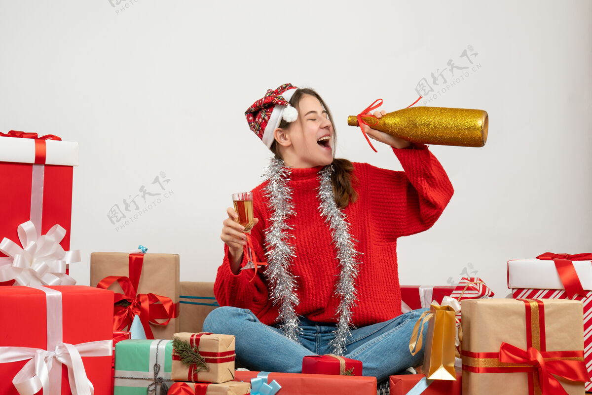 女孩戴着圣诞帽喝香槟的快乐派对女孩围坐在白色的礼物旁帽子坐着成人