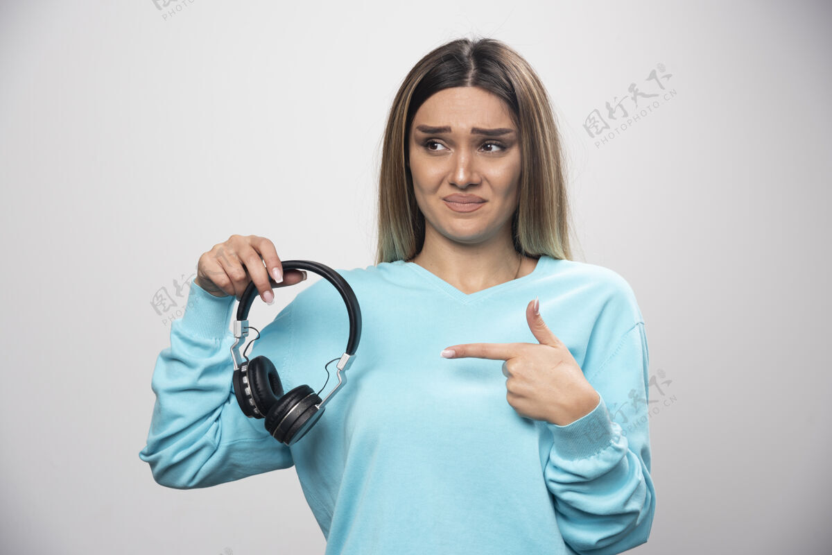 娱乐穿着蓝色运动衫的金发女孩听着耳机 却不喜欢音乐人音乐家不同意