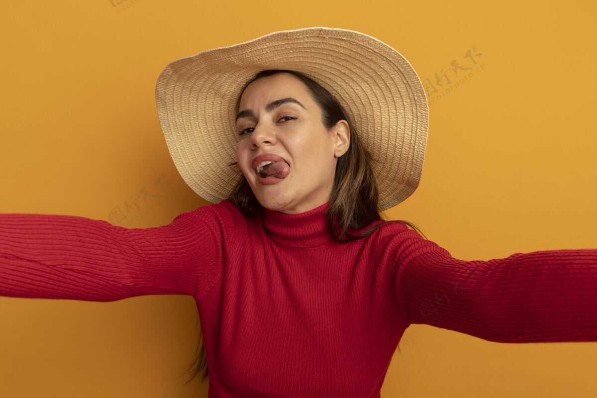 快乐快乐漂亮的高加索女人戴着沙滩帽伸出舌头摆姿势性感橙色