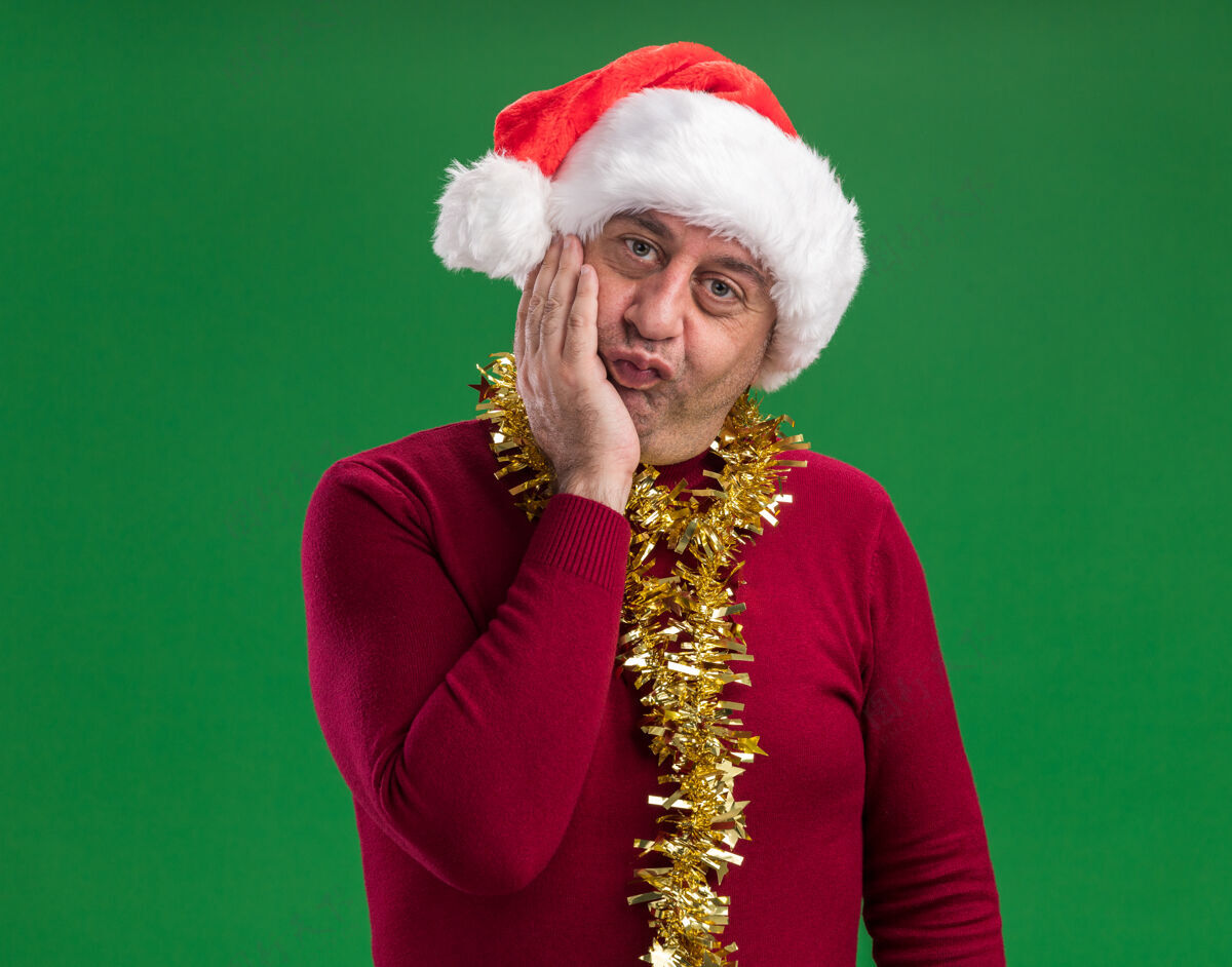 脖子中年男子戴着圣诞老人的帽子 脖子上戴着金属丝 站在绿色的背景下 幸福地看着相机圣诞老人周围圣诞节