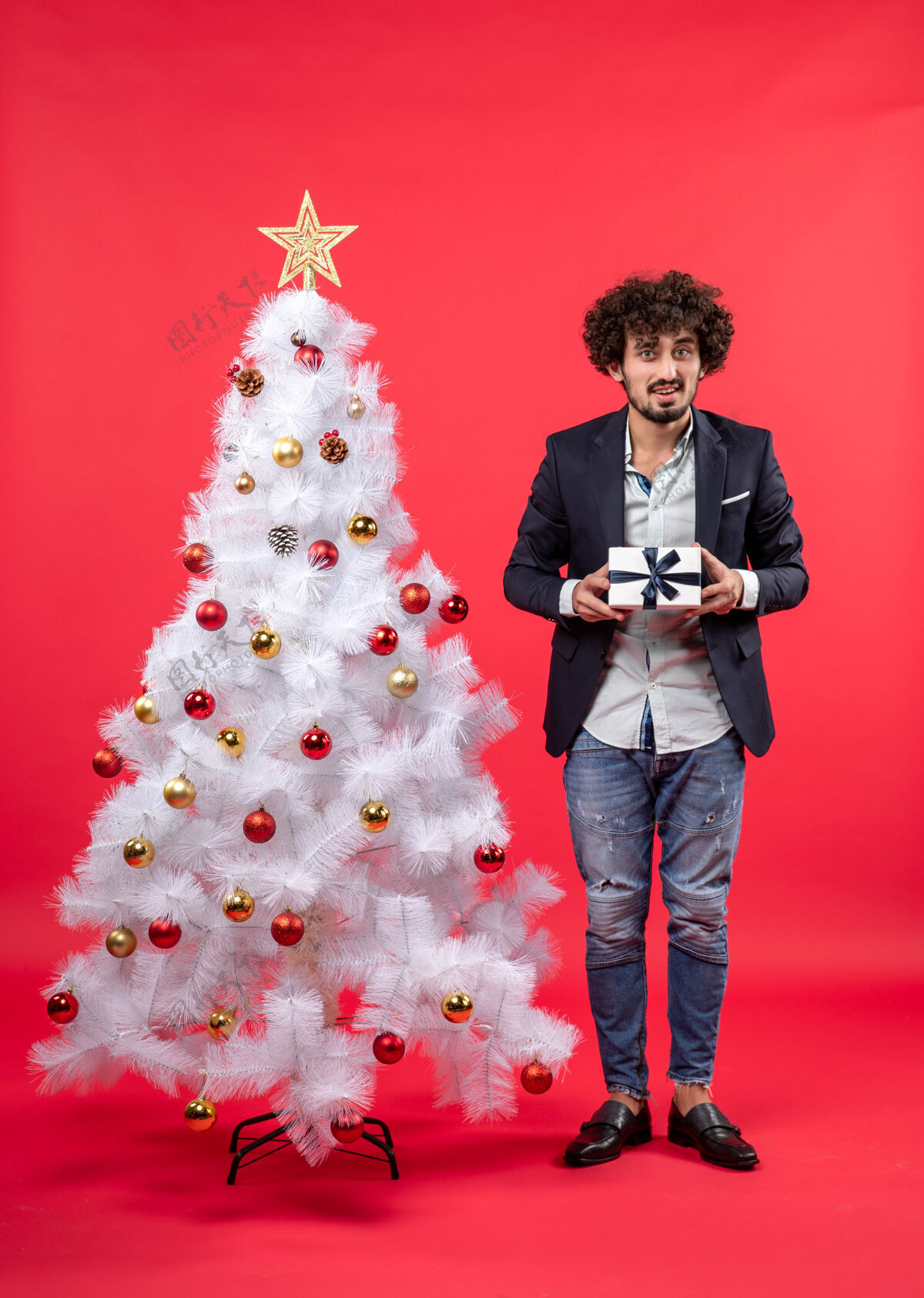 年轻人新年庆祝与年轻人举行的礼物附近装饰白色圣诞树上的红色镜头圣诞树礼物男人