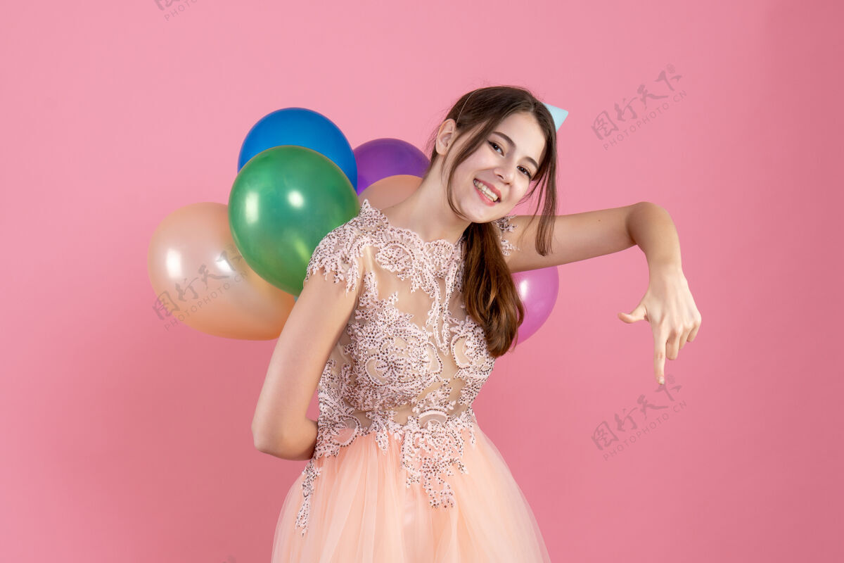 女孩戴着派对帽的派对女孩背着气球指着粉色的地面抱派对下