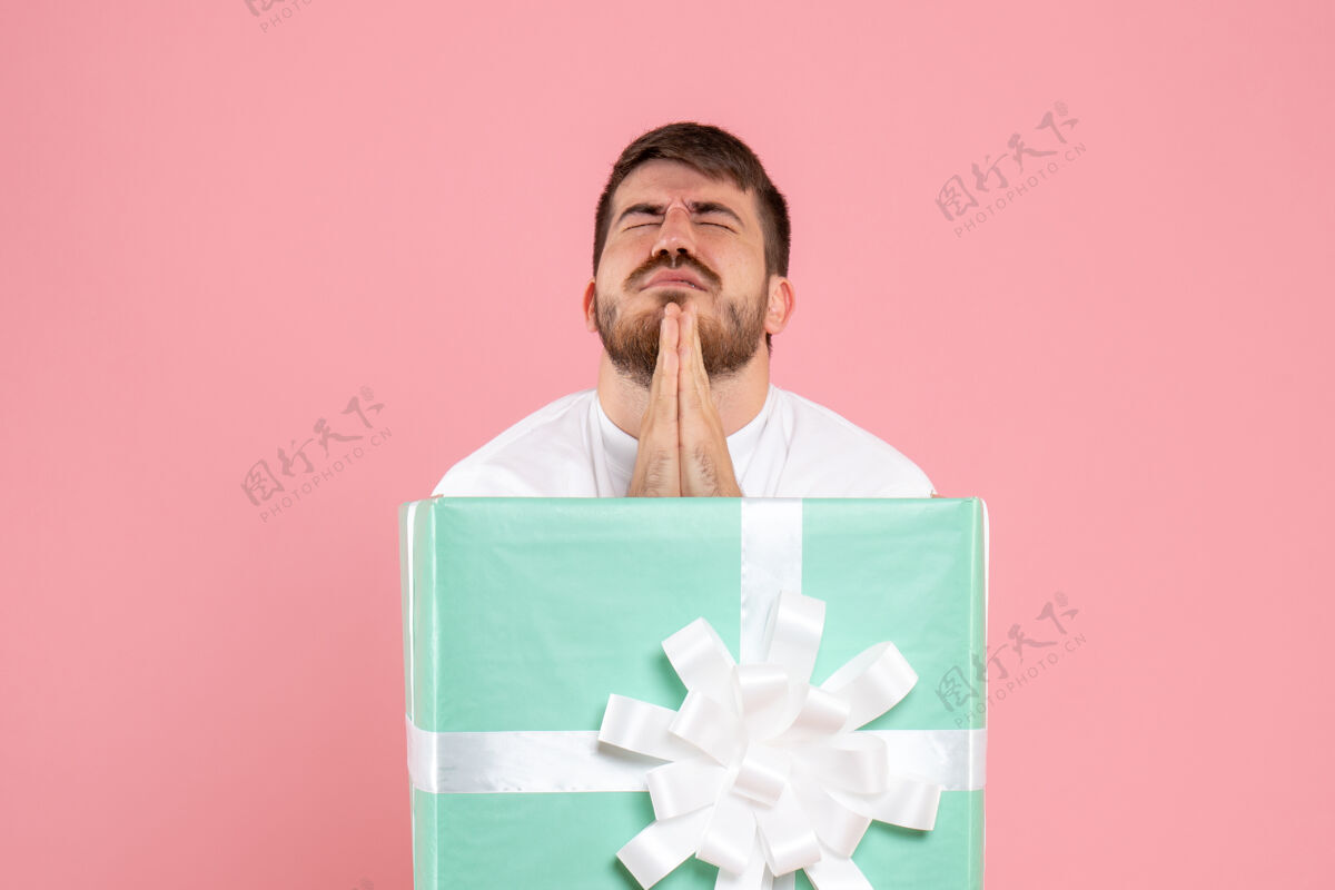 人礼物盒内的年轻人在粉红色墙上祈祷的正视图人年轻男性年轻