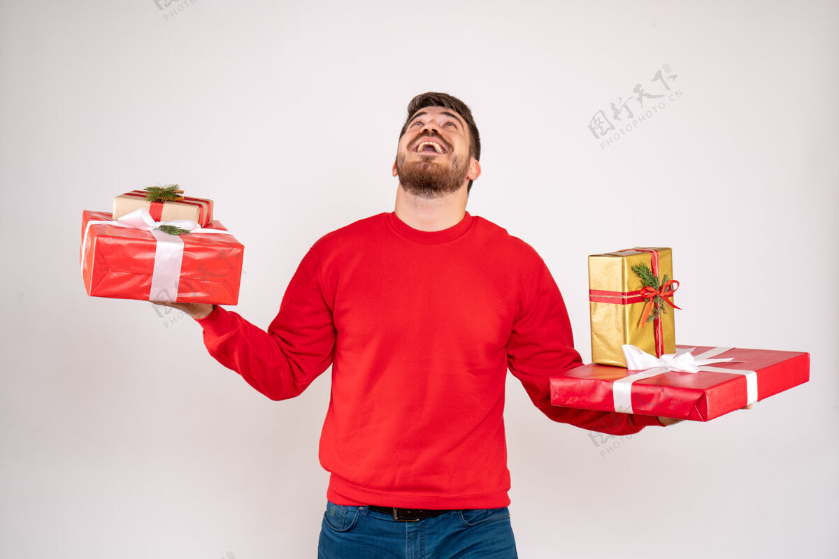 年轻男性身穿红衫的年轻人拿着圣诞礼物站在白墙上的正视图礼物圣诞节快乐