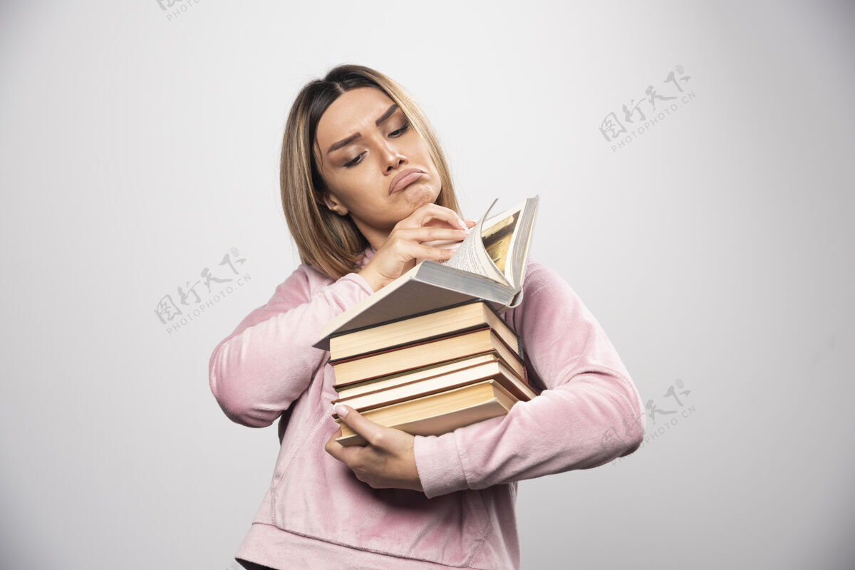 携带穿着粉色运动衫的女孩手里拿着一堆书 打开上面的一本读着学习年轻粉色