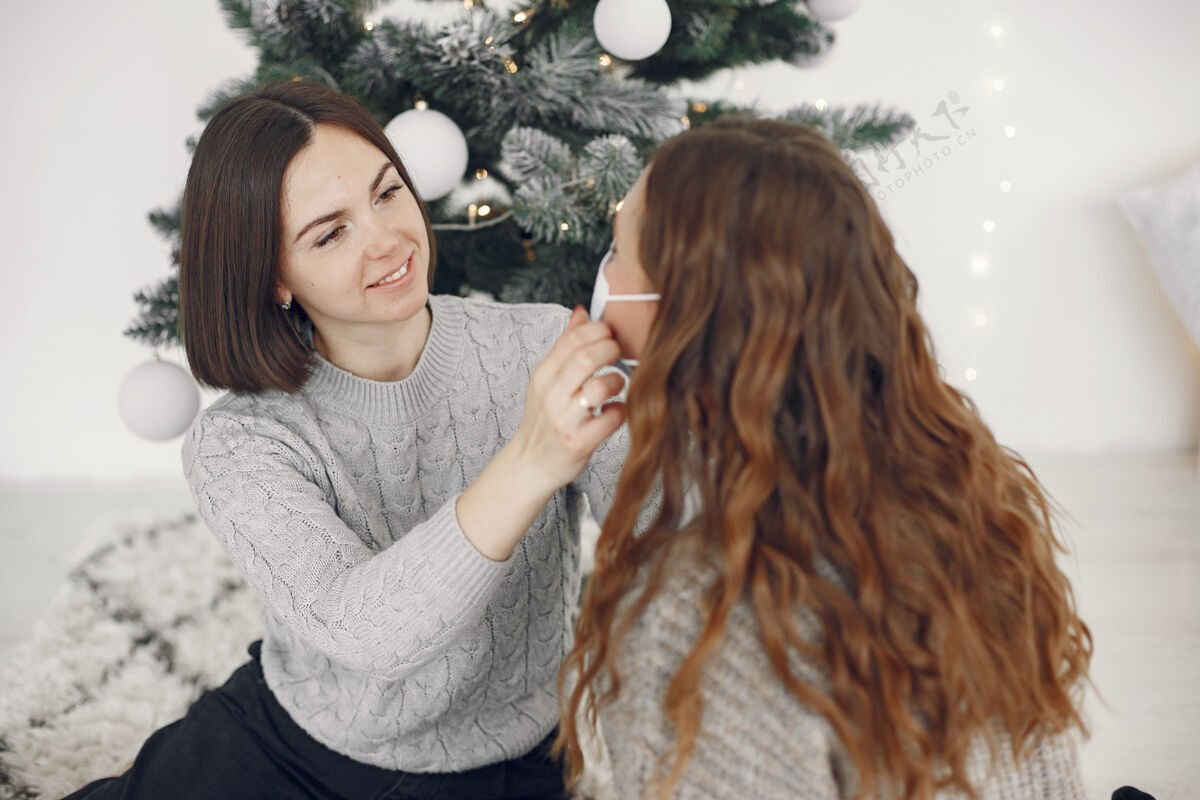 防护冠状病毒和圣诞节的概念女人帮她的朋友戴口罩流感肖像室内