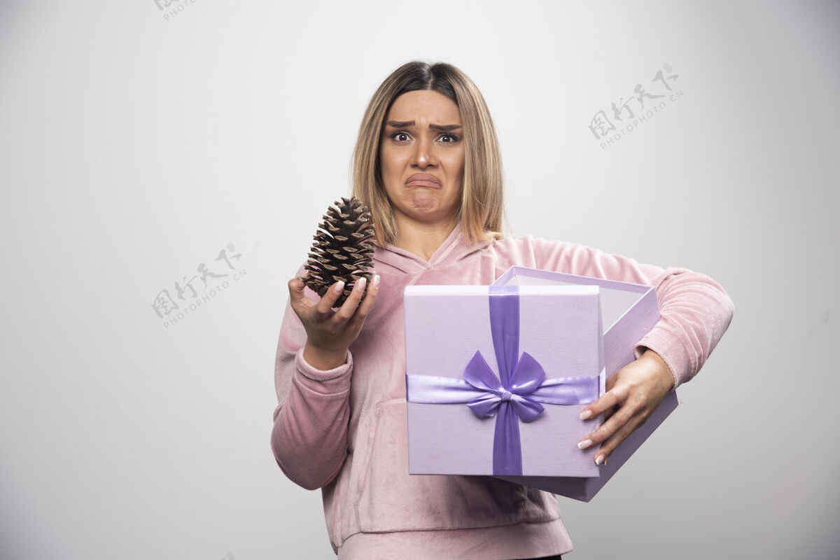 不喜欢穿着粉色运动衫的金发女士从礼盒里拿出一个橡树锥 感到不满意女性盒子人