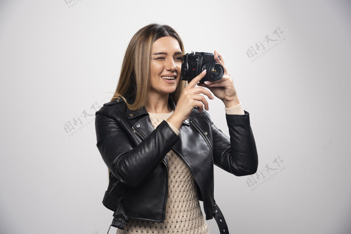 乐趣一位身穿黑色皮夹克的年轻女士 以积极微笑的态度用相机拍照快乐年轻人类