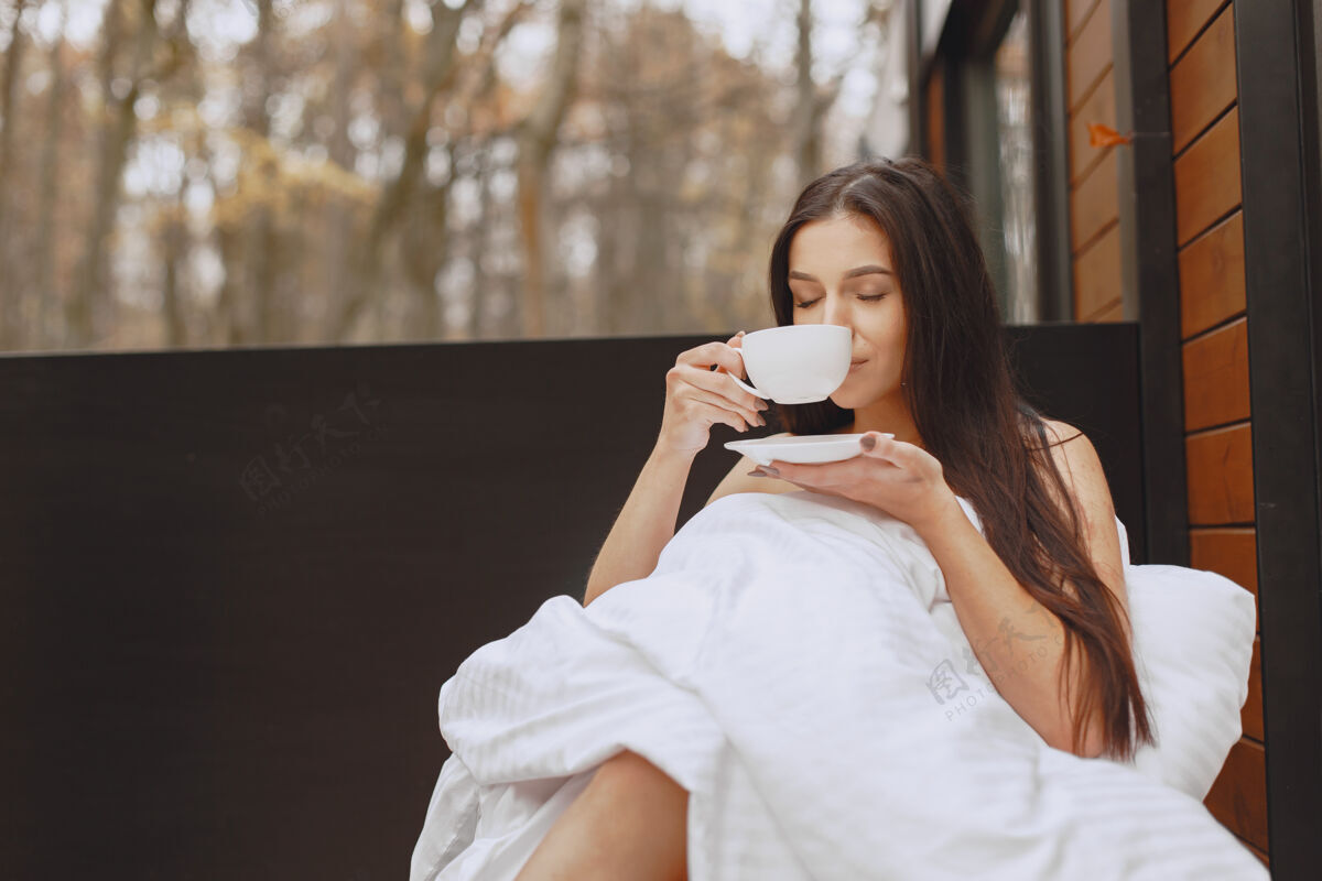 打开早上好穿着毯子的女人坐在露台上的女人黑发女人喝咖啡头发女士茶