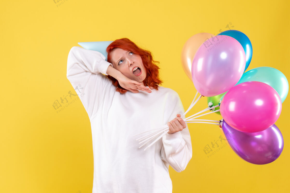 聚会黄色墙壁上手持彩色气球的年轻女子的正视图可爱生日快乐