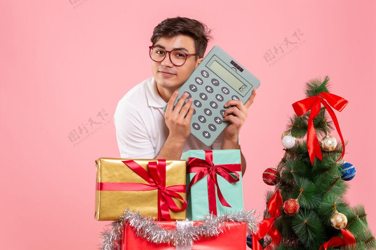 年轻男性圣诞节前后的年轻人手持计算器站在粉红色的墙上粉红色庆祝人