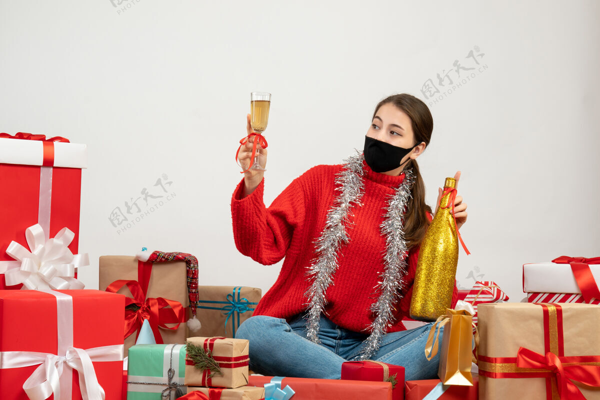 圣诞节戴着黑色面具的派对女孩拿着香槟瓶 围坐在白色的礼物旁敬酒人面具礼物