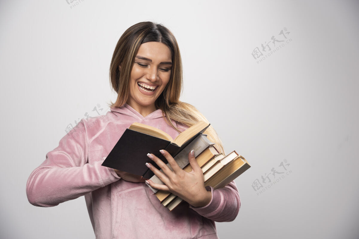 聪明一个穿着粉色衬衫的女孩手里拿着一堆书 打开上面的一本读着携带学习学生