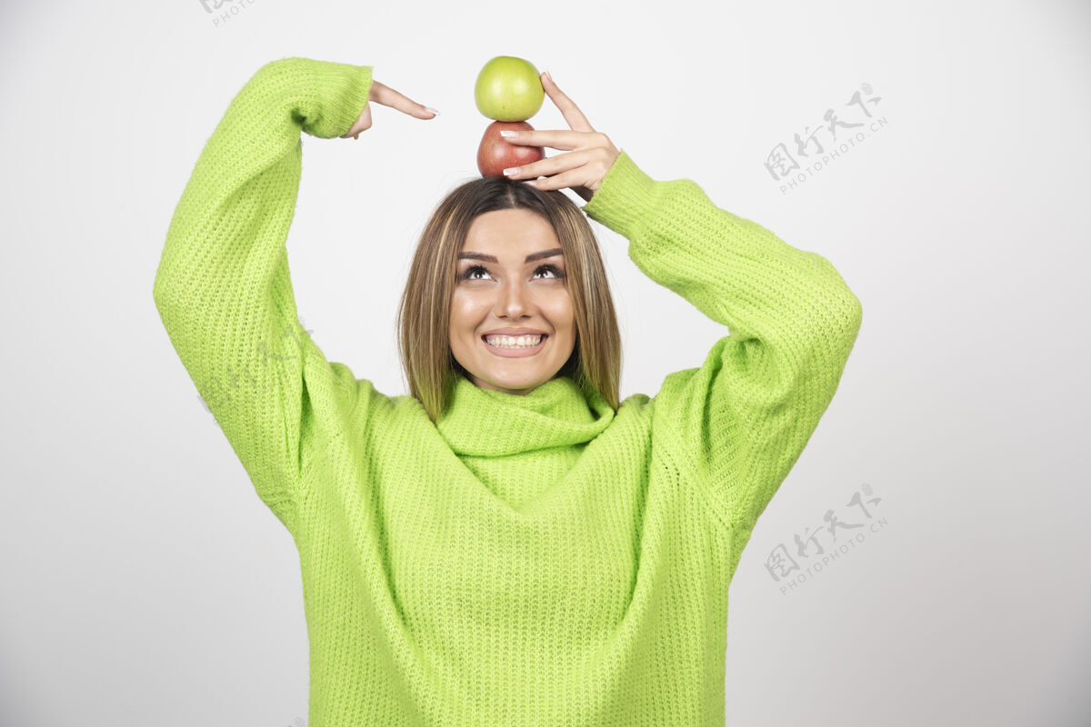 食欲身穿绿色t恤的年轻女子头顶举着两个苹果举行年轻苹果