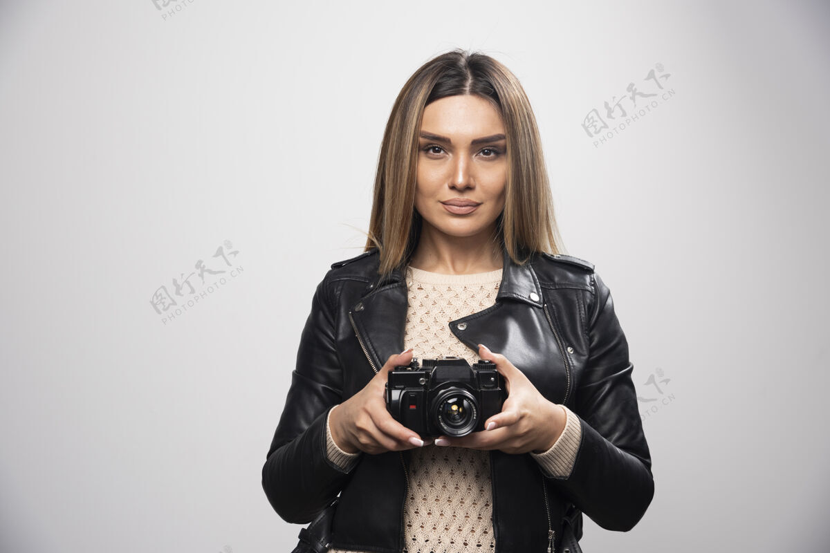 数码穿着黑色皮夹克的年轻女士严肃而专业地用相机拍照创意设备摄影
