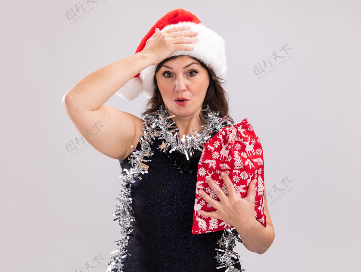 袋子遗憾的是 中年妇女戴着圣诞帽 脖子上戴着金箔花环 手里拿着圣诞礼物袋 看着相机 手放在头上 在白色背景上 留着复印空间手捧圣诞老人圣诞节