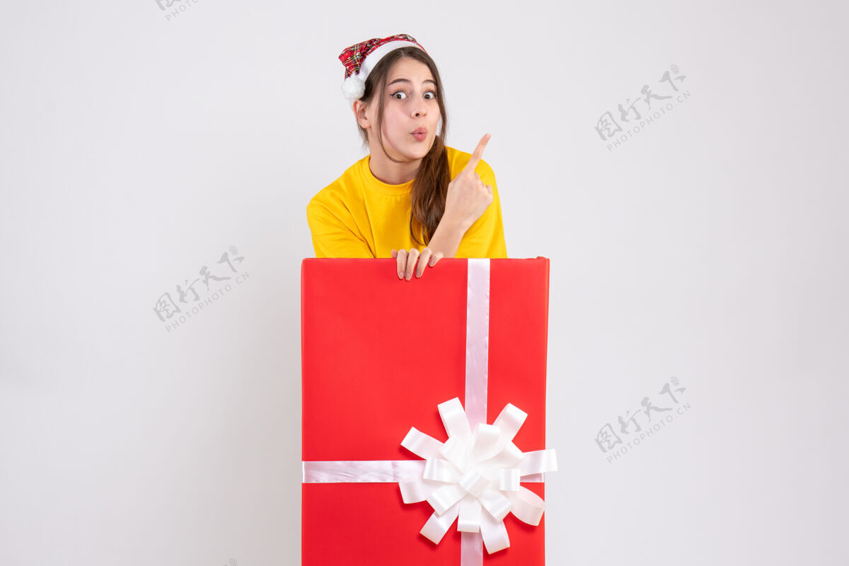 购物戴着圣诞帽的大眼睛女孩站在白色圣诞礼物后面帽子圣诞节礼物