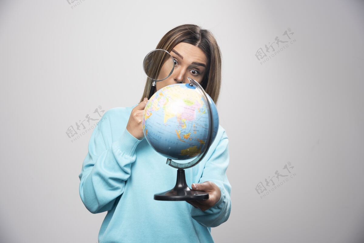 地点穿着蓝色运动衫的金发女孩拿着一个地球仪 用放大镜寻找目的地目的地摆姿势年轻人