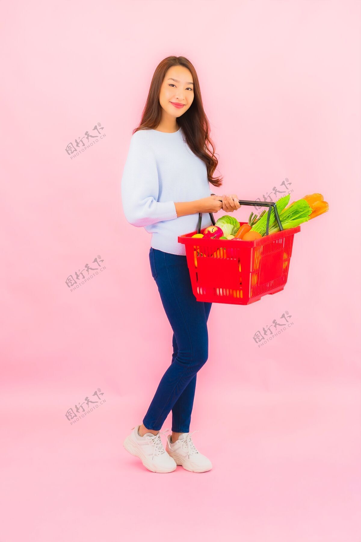 消费主义一幅美丽的亚洲年轻女子的画像 粉红色的隔离墙上 篮子里放着水果蔬菜和杂货有机商店电话营销
