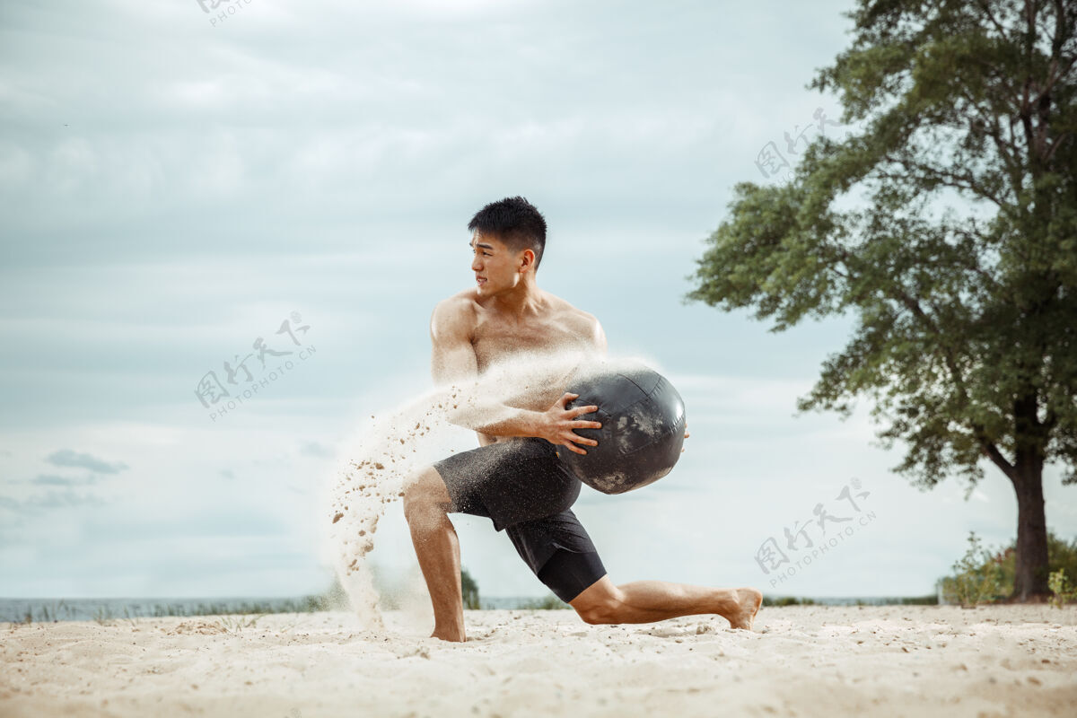 户外年轻健康的男子运动员在海滩上做深蹲白种人力量男性